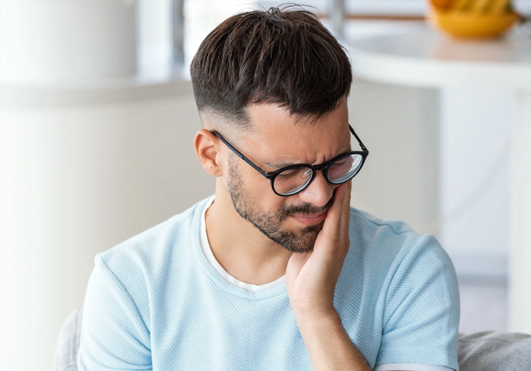 Man wearing glasses in light blue shirt resting head on hand, appearing thoughtful in modern office setting.