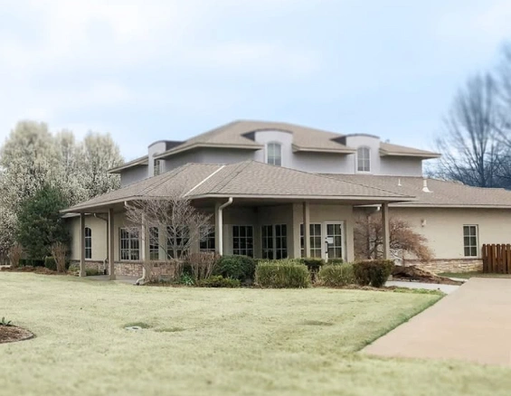 Large two-story residential home with manicured lawn and stone driveway in suburban setting.