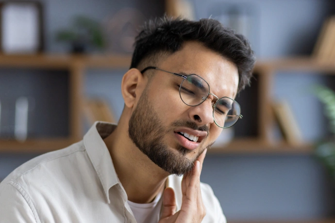 Smiling male dentist wearing glasses and white coat in modern dental office setting.