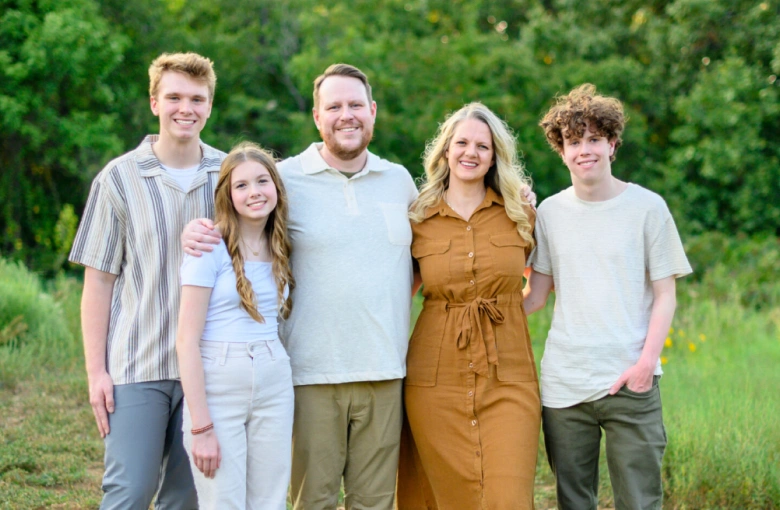 Five people standing together outdoors in casual clothing with green grass and trees in background.