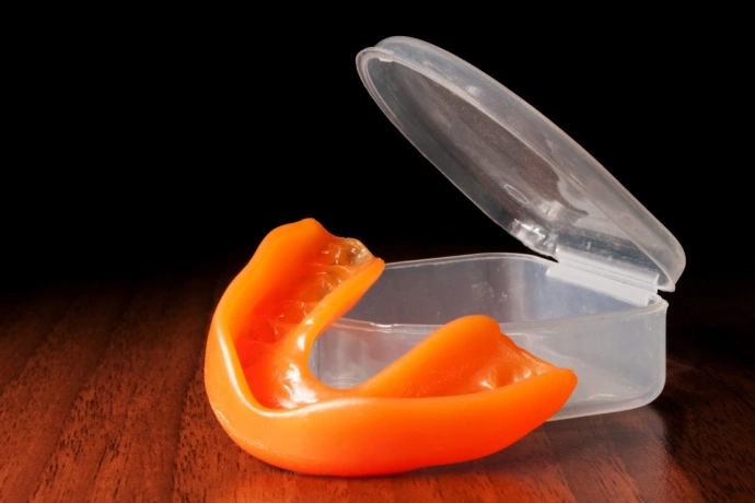 Orange peel resting in open clear container on wooden surface against dark background.
