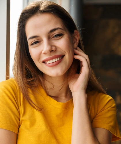 Smiling woman in yellow shirt with hand near face, professional dental studio portrait