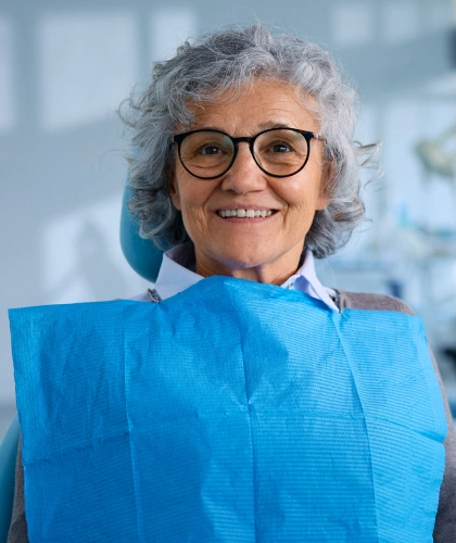 Smiling dental professional wearing glasses and blue protective gown in modern clinic setting.