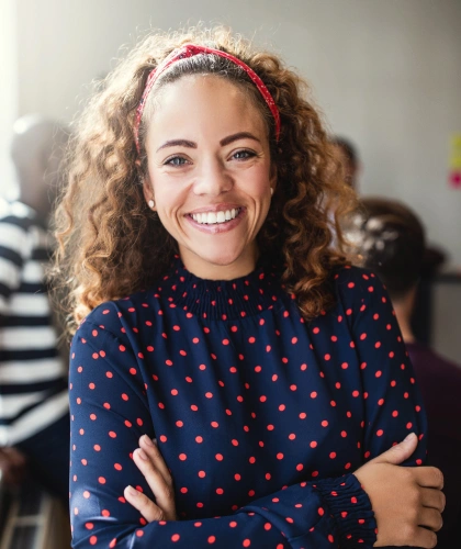 Woman with curly blonde hair wearing navy polka dot shirt, smiling at camera in dental office setting.
