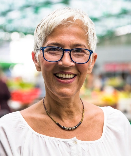 Smiling dental professional wearing glasses and necklace in front of blurred dental office background.