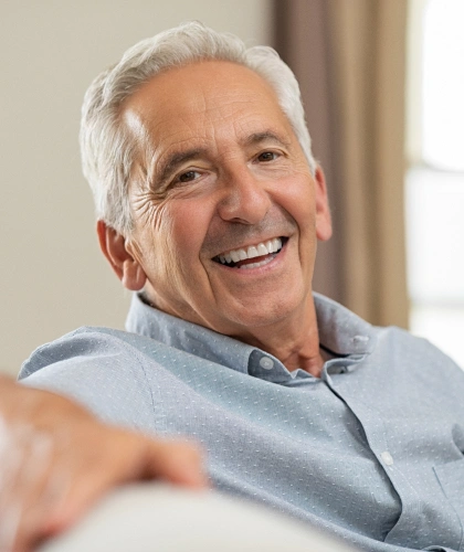 Smiling older man in light blue shirt, relaxed indoors setting, dental office environment.