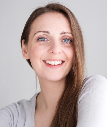 Woman smiling at camera in professional headshot against neutral gray background for dental studio.