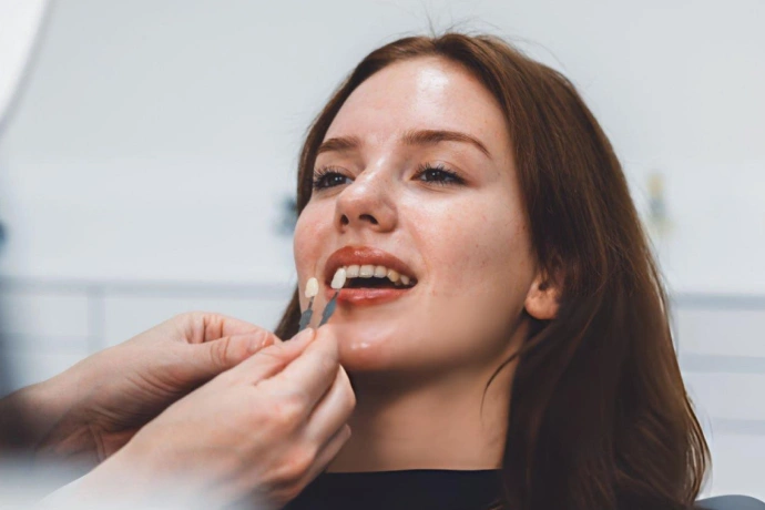 Woman applying red lipstick in bright, clinical setting with white background.