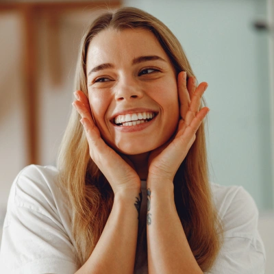 Happy woman smiling with hands on face in bright dental office setting.
