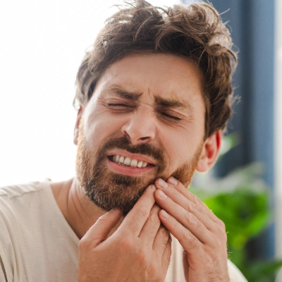 Man experiencing tooth pain, holding cheek outdoors in casual setting.