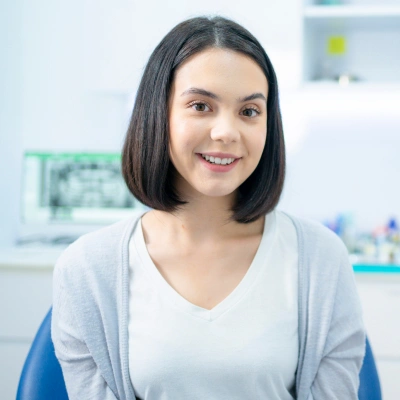 Smiling female dental professional in clinical office setting with blue chair visible