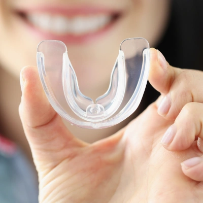 Person holding clear custom teeth whitening tray against blurred smile background