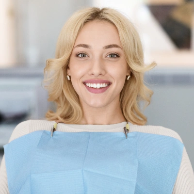 Professional woman smiling at camera, wearing light blue top in modern dental office setting.