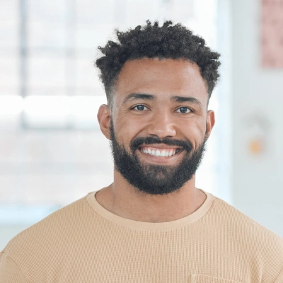 Smiling man in beige shirt, professional headshot in modern dental office setting.