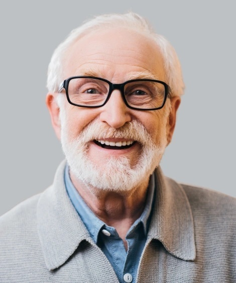 Smiling senior man with white hair and glasses wearing a blue shirt.